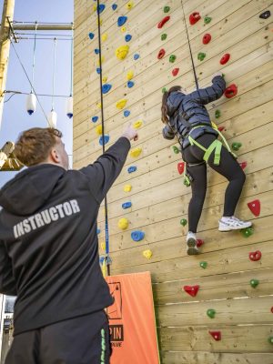 Climber on vertical climbing wall directed by an instructor.