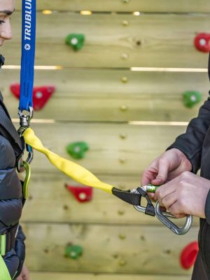 Instructor fits a guest with a safety harness for climbing wall activity.